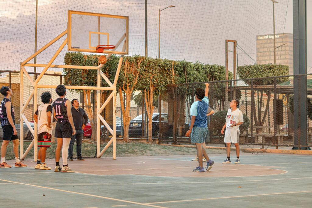 Players enjoy a lively street basketball game on an outdoor court at sunset.