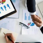 Business professionals handshake over graphs and charts in a corporate setting, symbolizing successful negotiation and agreement.